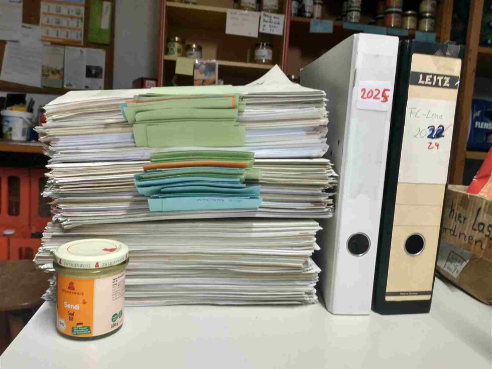 LeNa-Foodcoop - Tisch mit Stapel voller Rechnungen daneben Aktenordner