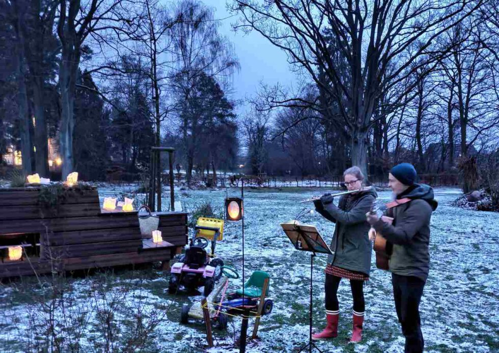 2 LeNa-Mitglieder musizieren mit Guitarre und Querflöte am Podest mit brennende Laternen